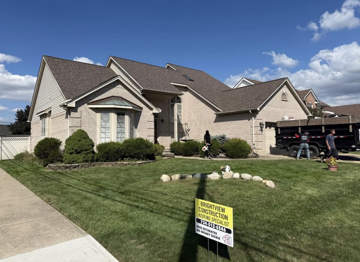 Completed brown and grey asphalt shingle roof on a large two story brick home with a BrightView Construction yard sign in the driveway