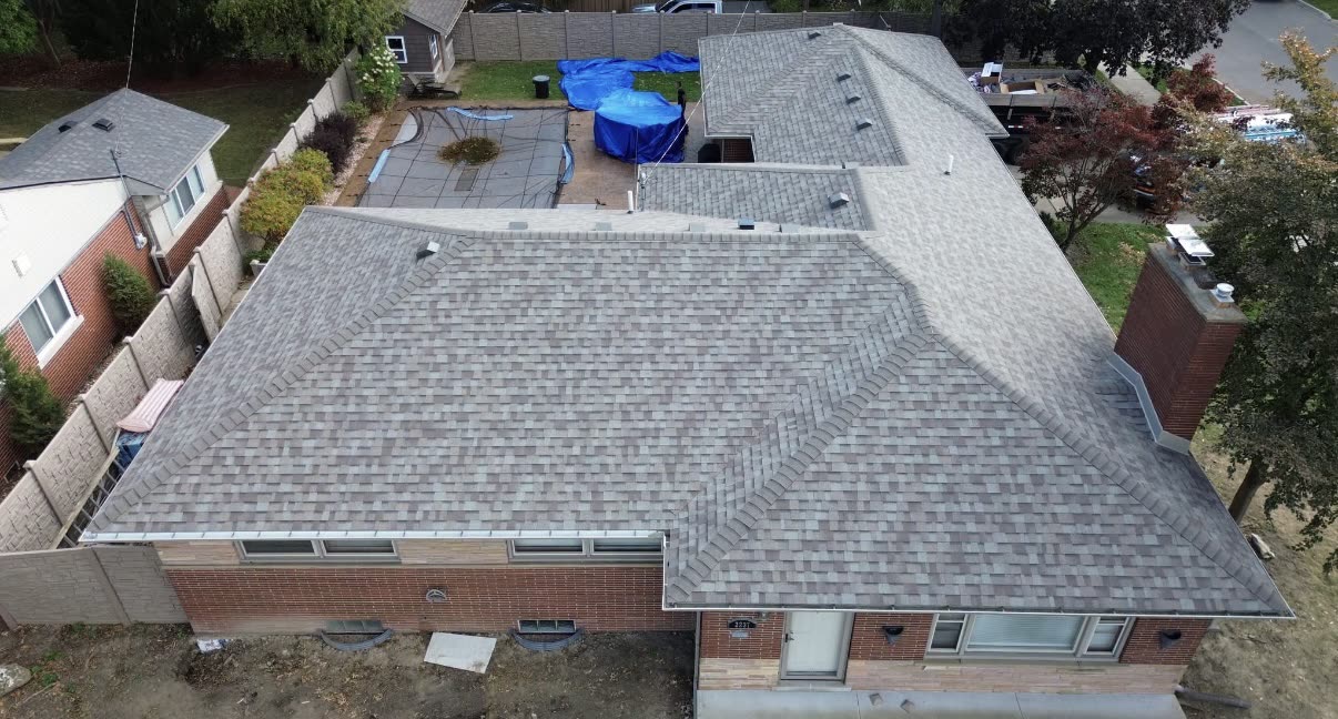 Aerial view of a completed shingle roof on a brick ranch home with the yard cleared of construction debris