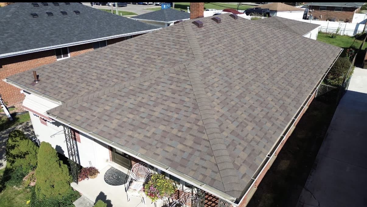 Completed grey and brown architectural shingle roof with a brick chimney and vents on a single story home