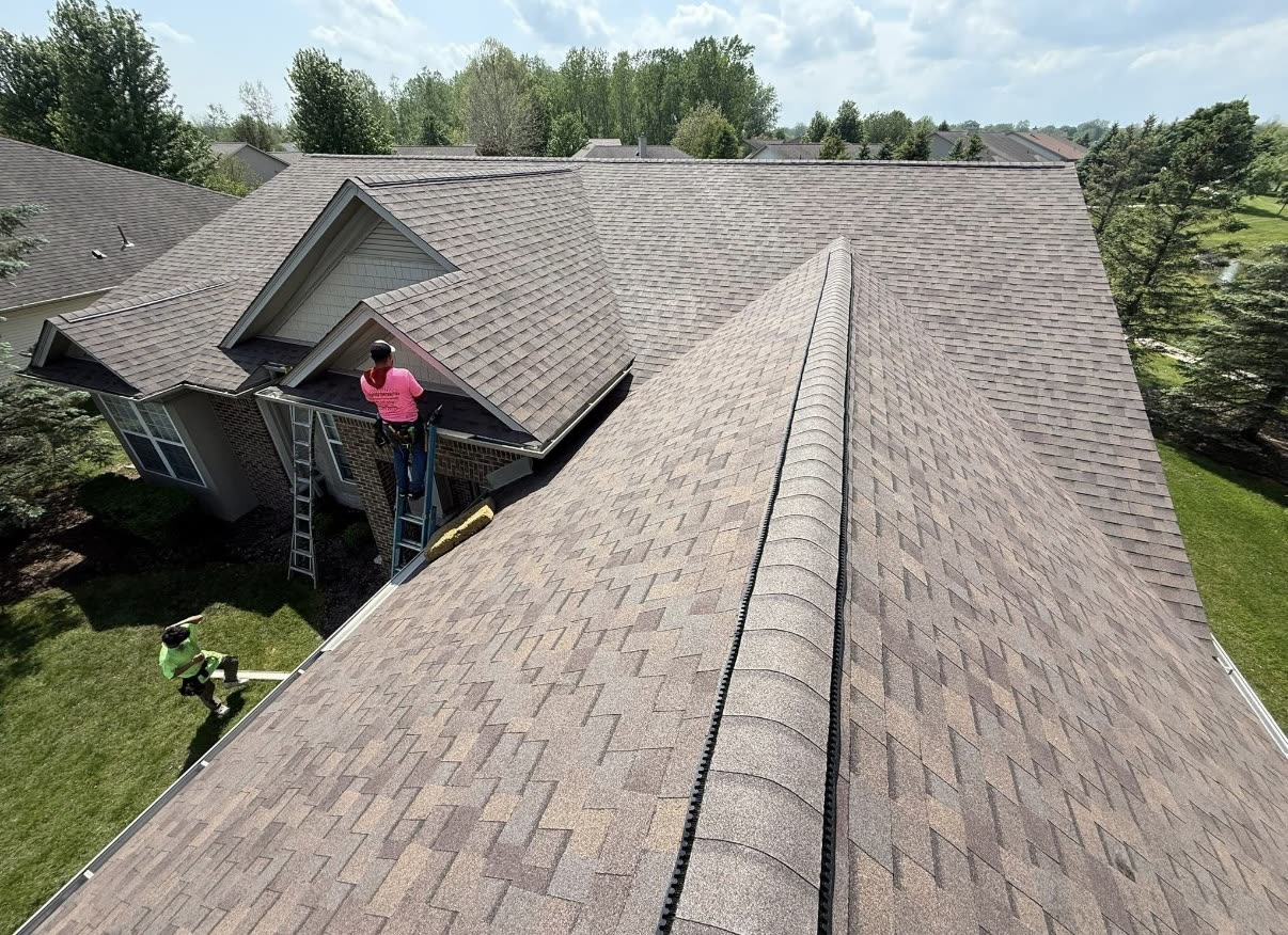 New dark charcoal architectural shingle roof with a ridge vent, beside a gable wrapped in synthetic house wrap