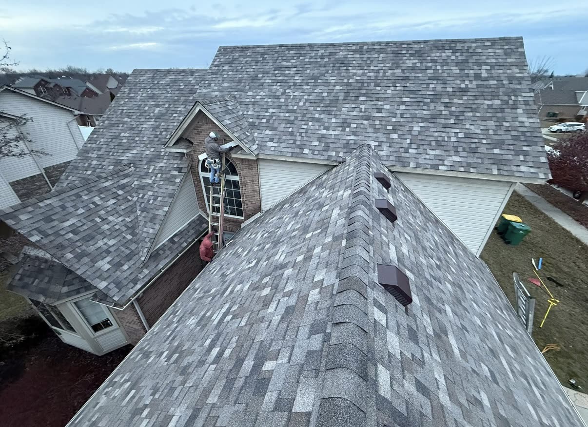 BrightView Construction roofer working on the peak of a large brick home roof at sunset