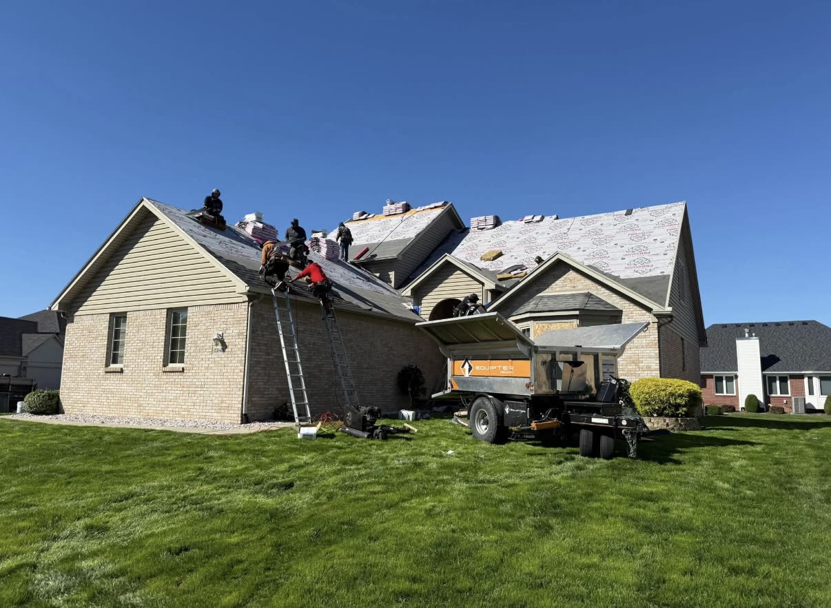 BrightView Construction crew installing synthetic underlayment over a stripped roof deck on a large brick home