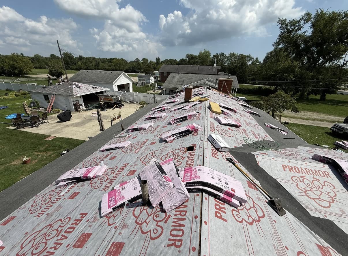 Aerial view of grey synthetic underlayment covering a residential roof deck with wrapped shingle bundles distributed across it